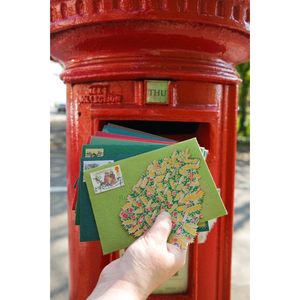 Hand placing colourful envelopes into a red postbox