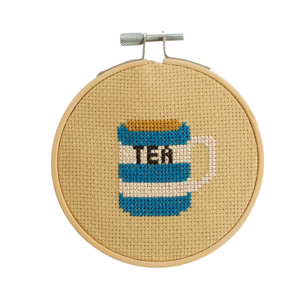 Cross-stitched tea can design in a wooden hoop on a white background
