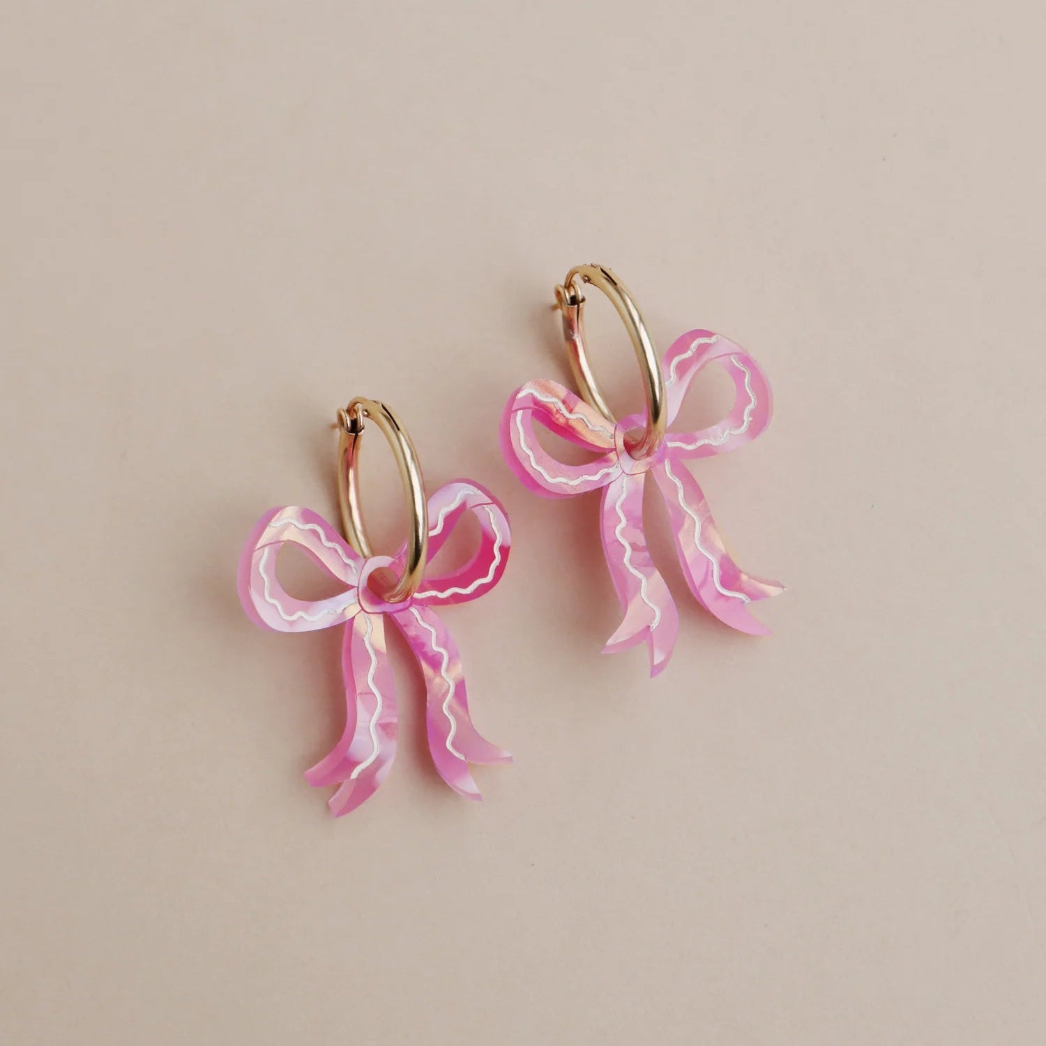 Pink bow earrings on a beige background
