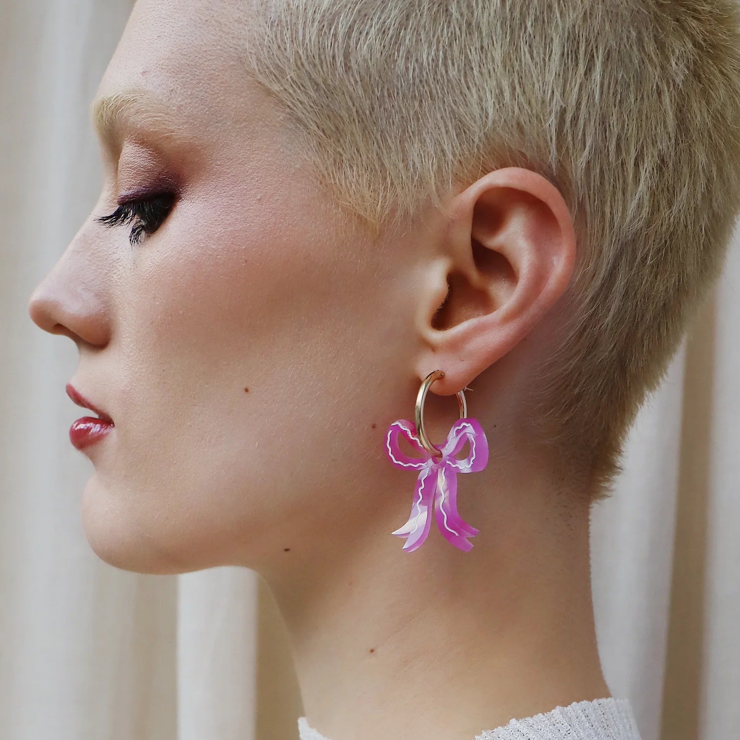 Woman wearing a pink bow earring with a neutral background