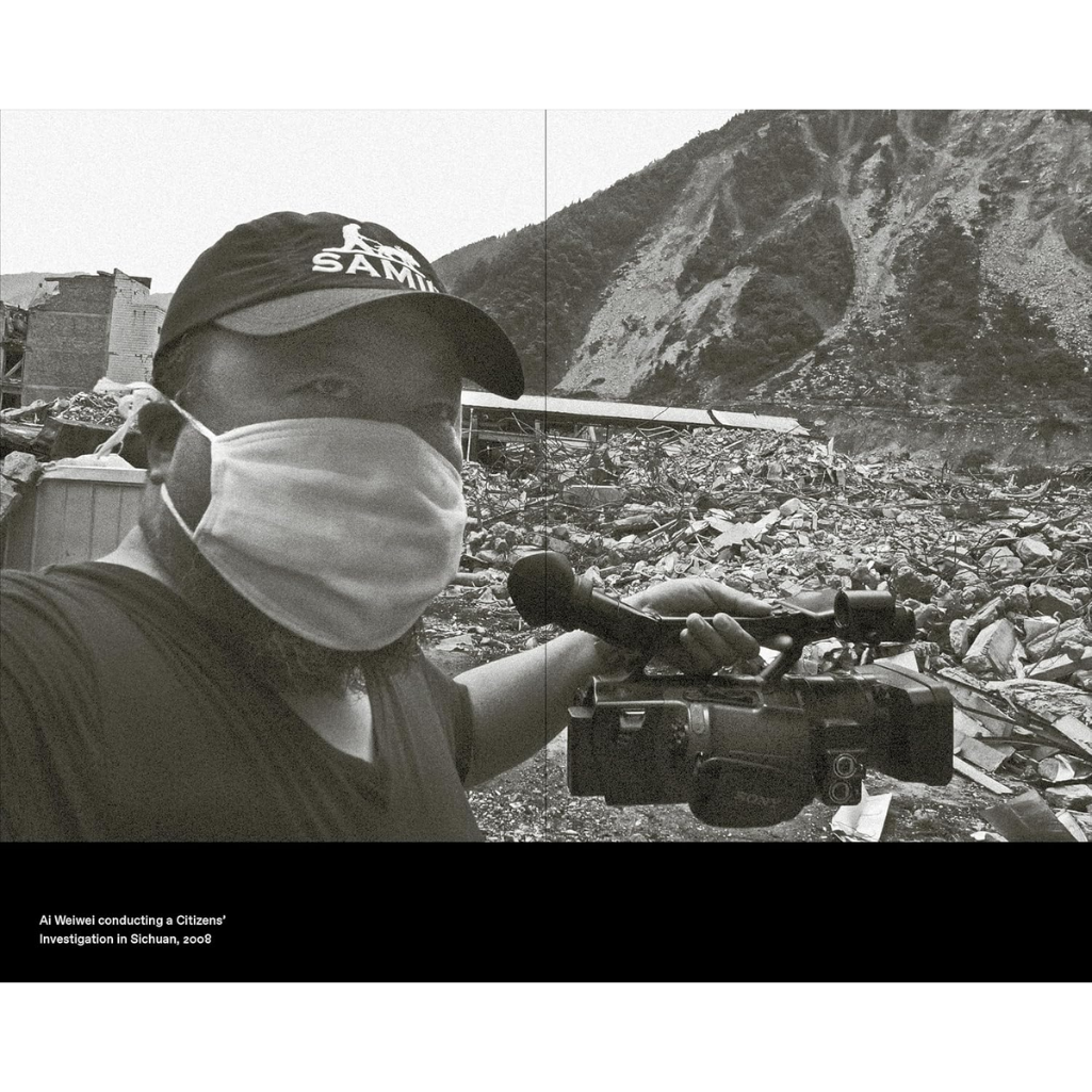 Person wearing a face mask and cap with 'Al Jazeera' branding, holding a camera in a disaster-stricken area.