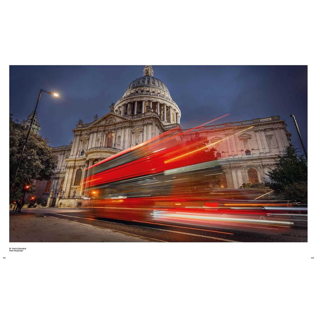A long-exposure photograph of St. Paul's Cathedral in London at night, featuring vibrant red and white light trails from passing buses in the foreground.