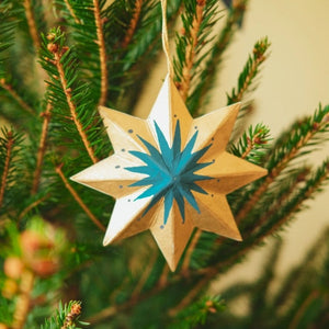 Star-shaped wooden ornament with blue center hanging on a Christmas tree branch.