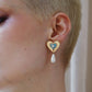 Heart-shaped earring with a pearl drop worn by a person with short hair.