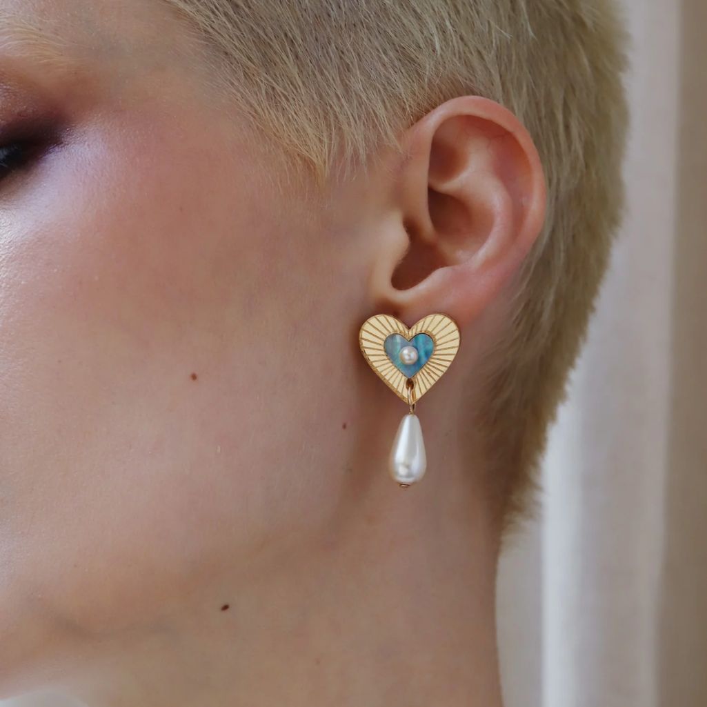Heart-shaped earring with a pearl drop worn by a person with short hair.