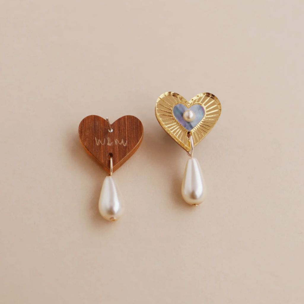 Two heart-shaped earrings with pearl drops on a beige background