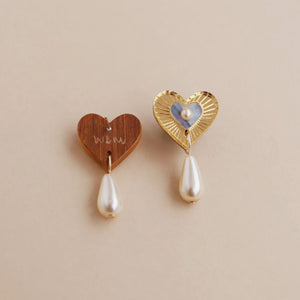 Two heart-shaped earrings with pearl drops on a beige background