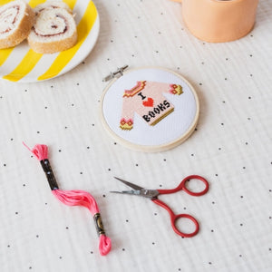 Cross-stitched hoop with 'I love books' design on a polka dot tablecloth with embroidery floss and scissors.