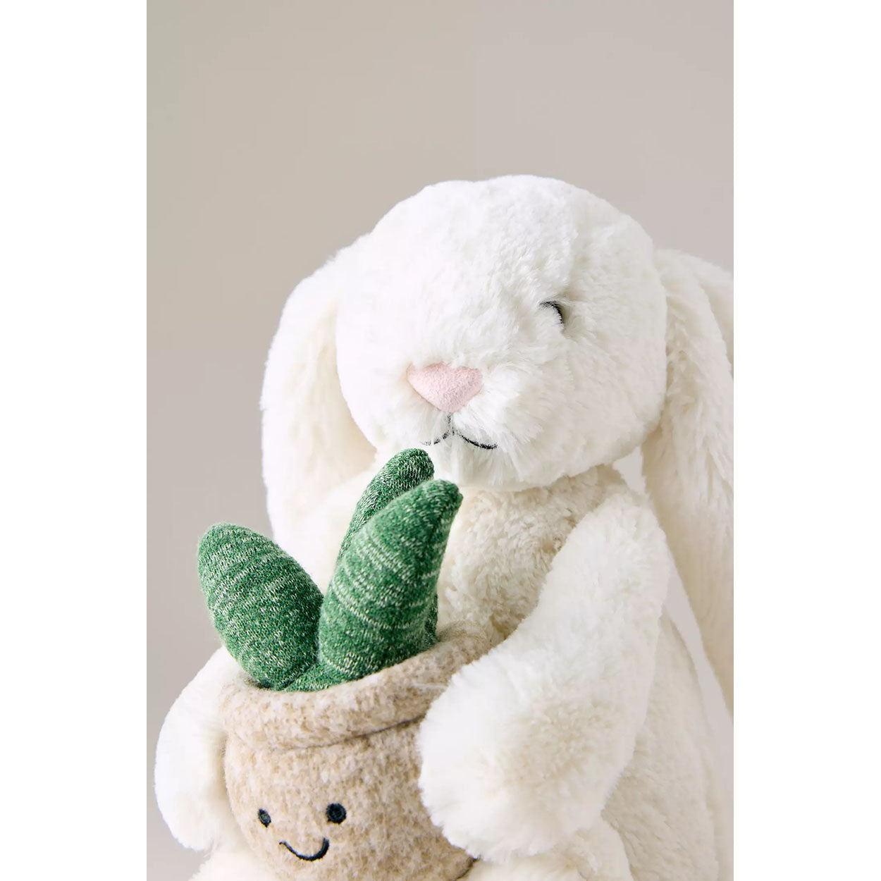Plush toy rabbit holding a small potted plant with a smiling face against a neutral background