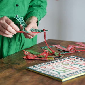 Person in a green shirt working with colourful paper crafts on a wooden table.