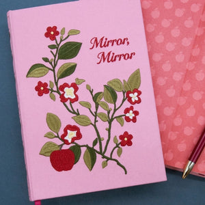Pink notebook with floral design and 'Mirror, Mirror' text on a blue surface