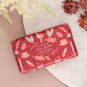 Red soap packaging with Jane Austen design on a textured surface with flowers.