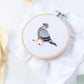 Cross-stitched bird design in an embroidery hoop on a white fabric background