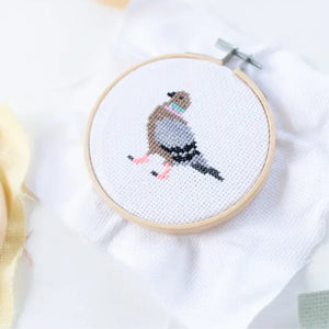 Cross-stitched bird design in an embroidery hoop on a white fabric background