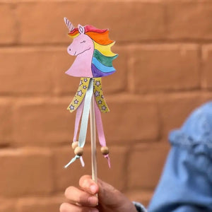 Colorful unicorn-shaped wand held by a person against a brick wall.