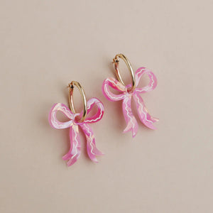 Pink bow earrings on a beige background